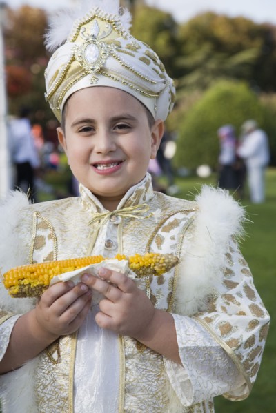 Istanbul, Turkey. Sultanahmet. Young boy eating sweetcorn cooked on the cob wearing traditional