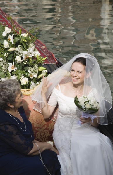 Venice, Veneto, Italy. Smiling bride in wedding dress and veil carrying bouquet seated beside