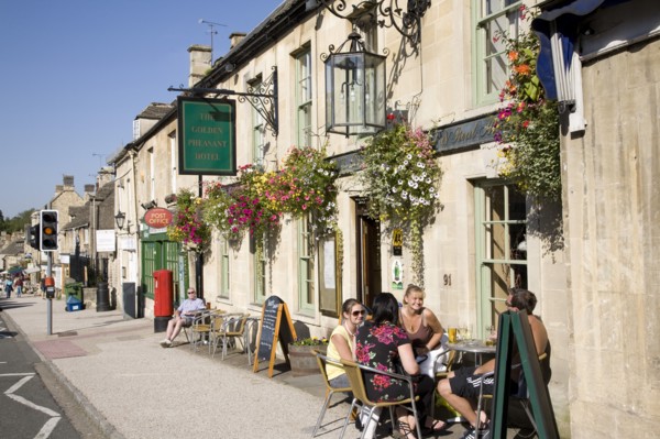 Burford, Gloucestershire, England. Tourists sat outside the Golden Pheasant Hotel in the Cotswolds.