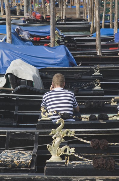 Venice, Veneto, Italy. Gondolier in striped shirt using mobile phone while sitting in one of a line