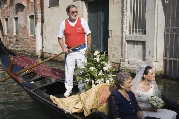 Venice, Veneto, Italy. Gondolier steering decorated gondola carring bride in wedding dress and veil