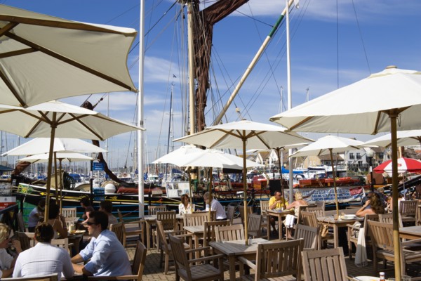Port Solent People at restaurant tables under sun shade umbrellas with yachts moored in the marina