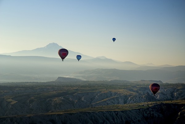 Early morning with hot air balloons in flight above tufa landscape with Mount Erciyes in the