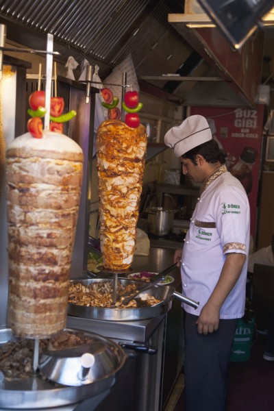 Turkey, Istanbul, Sultanahmet man in kebab restaurant carving shawarma from skewered meats. 
Photo