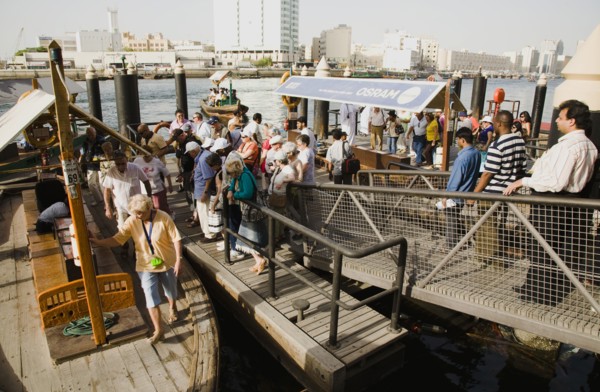 Tourists board Abra water taxi moored on the Creek with Bur Dubai heritage skyline behind.