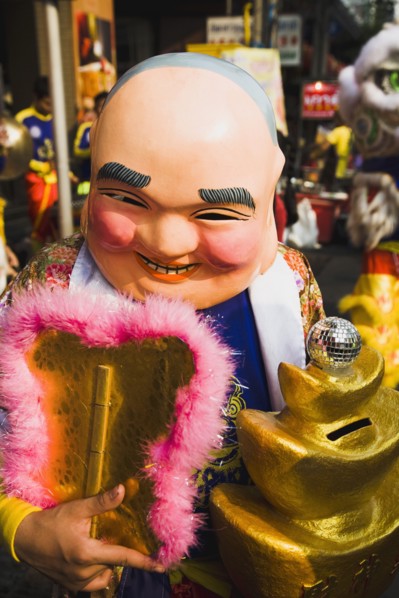Member of dance troupe with papier mache character head and fan collecting money for Chinese New Year show.