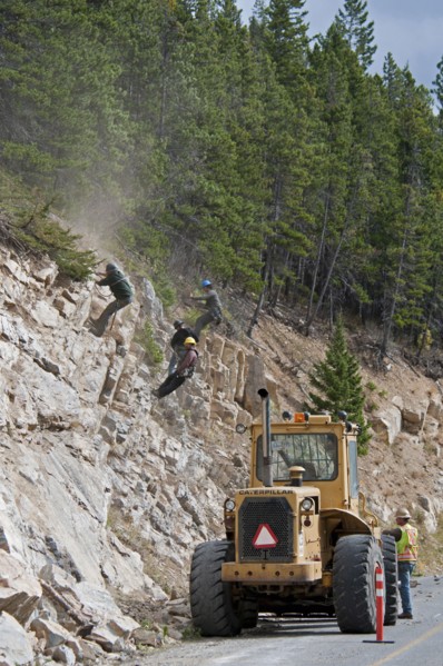 Workers wearing safety helmets on ropes clearing a rock slide and making the rock face safe along the Akamina Parkway Caterpillar tractor on parkway