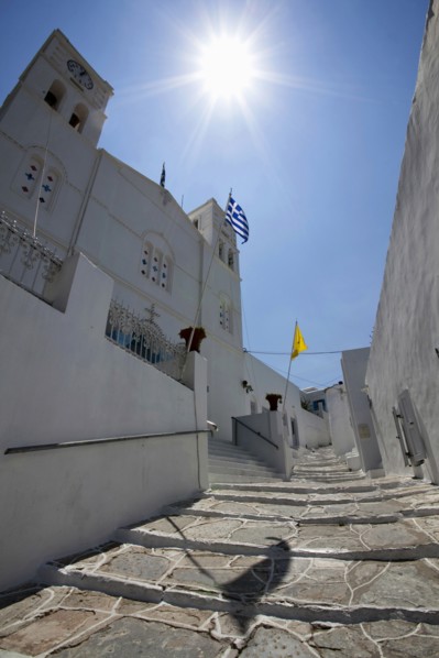 Portrait format low angle photograph of a typical alley found only at Cyclades island complex with the church of Agios Spyridonas on the left hand side.