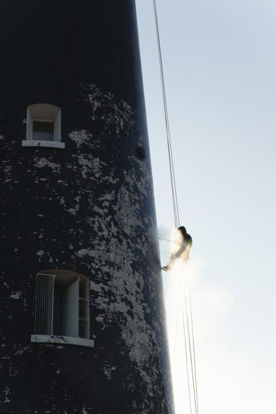 Man cleaning Lighthouse tower with pressure washer whilst abseiling.