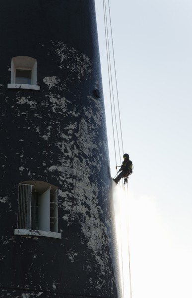 Man cleaning Lighthouse tower with pressure washer whilst abseiling.