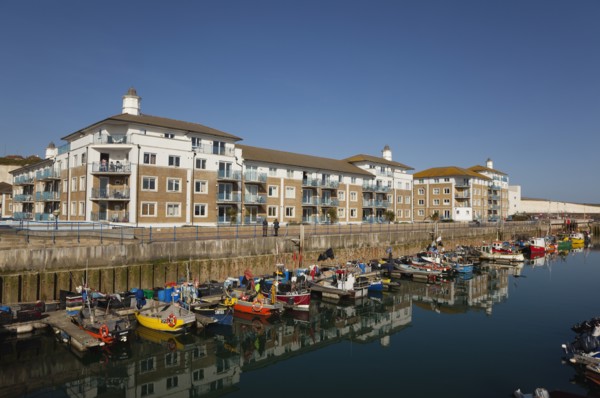 View over fishing boats moored in the Marina with apartment buildings behind.