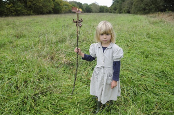5 year old Eva with stick & leaf flag in a field of grass.