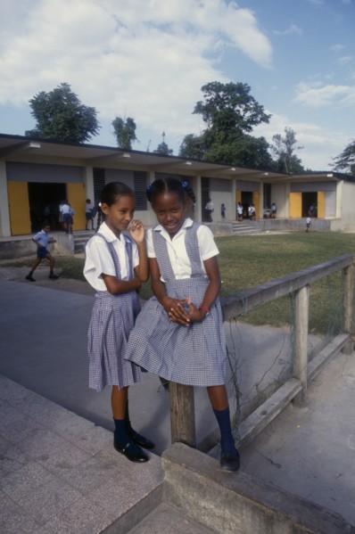 West Indies, Jamaica, Education, Two schoolgirls in checked dresses in playground in front of