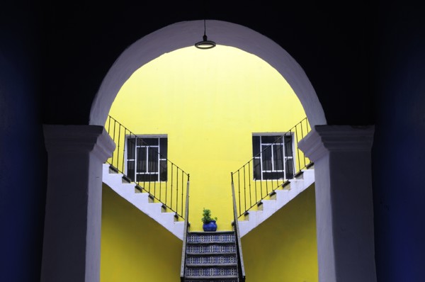 Mexico, Puebla, Looking into inner courtyard through archway in shadow towards yellow painted wall