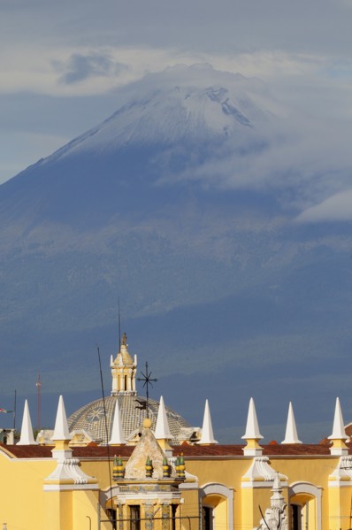 Mexico, Puebla, View of volcanic peak of Popocatepetl wreathed in cloud with Puebla rooftops in