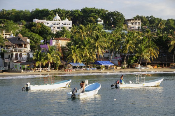Mexico, Oaxaca, Puerto Escondido, Fishing boats in bay at Playa Marinero lined with cafes bars and