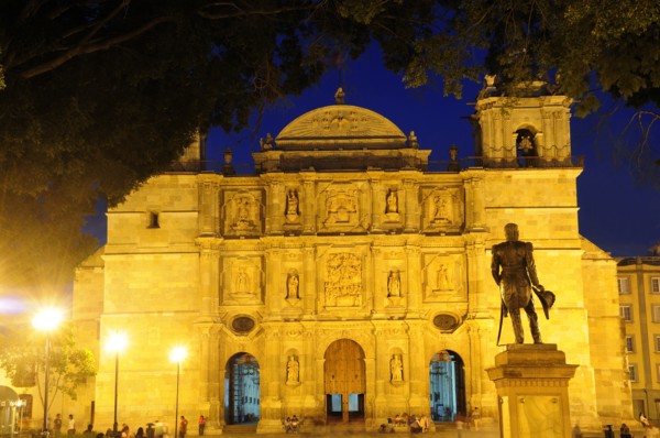 Mexico, Oaxaca, Baroque exterior facade of cathedral at night part framed by tree branches with