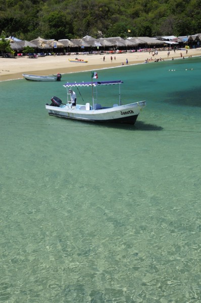 Mexico, Oaxaca, Huatulco, Playa La Entrega Tour boat moored in clear shallow water in foreground of