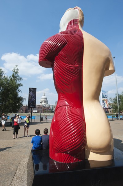 Two children pose for a photograph in front of Damian Hirst's sculpture, 'Hymn', the South Bank, Londonn