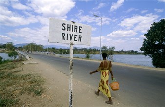 WOMAN WALKING PAST SIGN, SHIRE RIVER, MALAWI