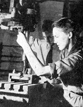 Woman in tank factory being instructed in the use of a metal power drill