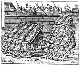 Roman soldiers forming a Tortoise with their shields and approaching the walls of a besieged fortress
