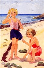 Girls playing with shells on a sandy beach on their seaside holiday