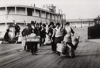 Imigrants to US landing at Ellis Island circa 1900. They head for the processing centre carrying