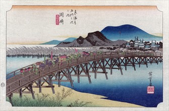 Bridge at the Okasaki station with porters and attendants carrying sedan chair and bundles