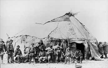 Native American men and children standing in front of a large tent structure