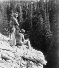 Two Native Americans looking over the edge of a cliff