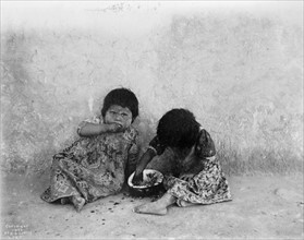 Two Hopi girls seated on ground eating melon