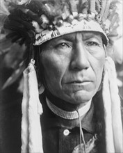 Head-and-shoulders portrait of a Nez Percé man in full feather headdress
