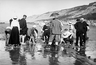 French coastal scene showing young children and adults searching a beach for shellfish or crabs