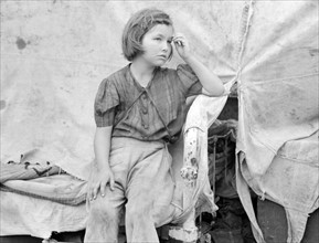 Child of migrant worker sitting on bed in tent home of cotton picking sacks