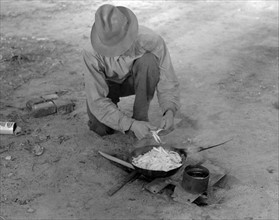 Migrant worker cooking meal over campfire, 19390101 .