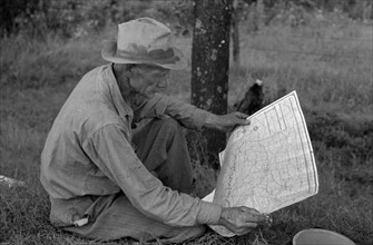White migrant agricultural worker from Texas studying the map while stopped for lunch on the roadside 19390101