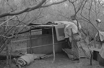 White migrant worker living in camp with two other men, working on lean-to which is to be his sleeping quarters. Near Harlingen, Texas 19390101.
