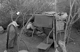 White migrant worker living in camp with two other men, working on lean-to which is to be his sleeping quarters. Near Harlingen, Texas by Russell Lee, 1903-1986, dated 19390101.