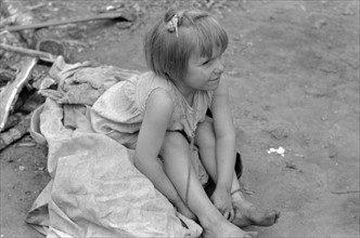 Child of white migrant worker sitting on cotton pickers' sacks near Harlingen, Texas by Russell Lee, 1903-1986, dated 19390101.