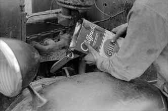 Migrant worker pouring oil into motor of automobile near Harlingen, Texas by Russell Lee, 1903-1986, dated 19390101.