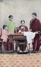Print depicting an Indian woman using a Singer sewing machine to sew a garment whilst her daughters look on