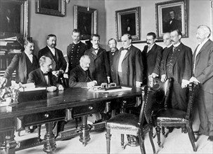 Photograph of French Ambassador Pierre Paul Cambon signing the Peace Protocol, as President William McKinley and others watch