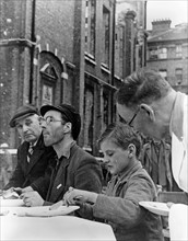 American egg and bacon being enjoyed, by workmen and boys, at a feeding centre in England during world war two.