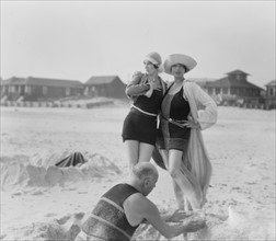 Unidentified man building sand castle and two women, Long Beach, New York 1910