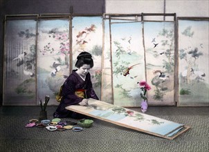 Hand-coloured photograph of a Japanese woman painting a screen by Felice Beato