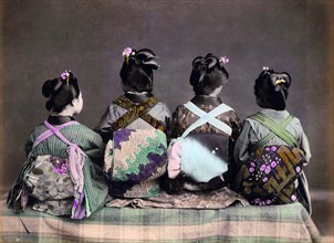 Hand coloured photograph of Geishas sitting with their backs toward the camera
