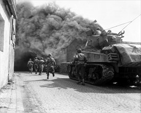 Photograph of M4 Sherman tank move through a smoke filled street in Wernberg