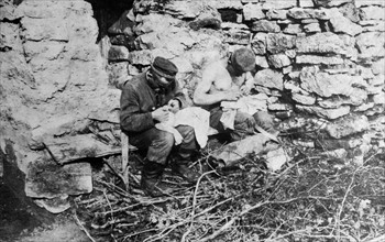 Photograph of German soldiers hunting for lice on their clothing in the trenches