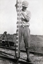 Rodman holding rod vertical during marine oceanographic observations.1900